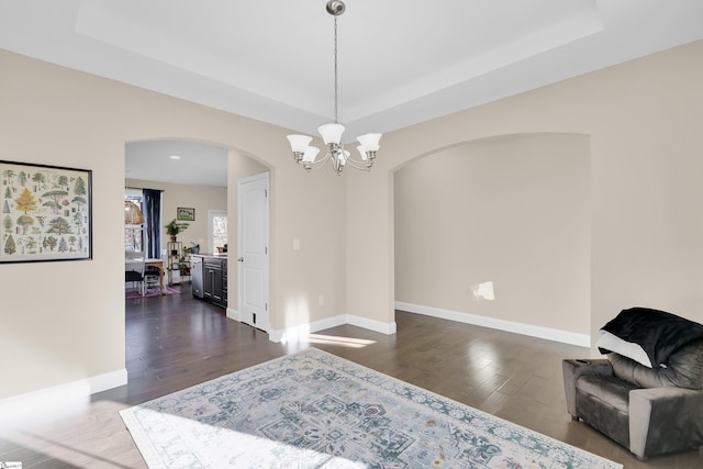 dining space with dark wood-type flooring, a chandelier, and a tray ceiling