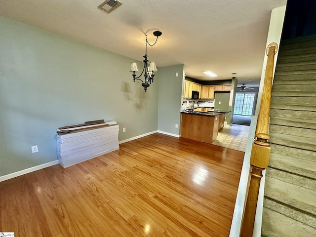 interior space with ceiling fan with notable chandelier and light hardwood / wood-style flooring