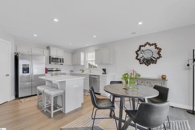 kitchen featuring appliances with stainless steel finishes, white cabinetry, a center island, decorative backsplash, and light wood-type flooring