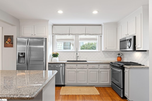 kitchen with sink, white cabinets, stainless steel appliances, light stone countertops, and light hardwood / wood-style flooring