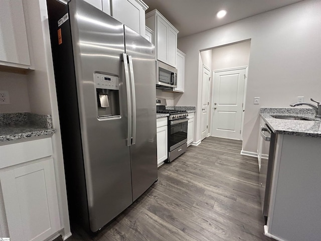 kitchen with appliances with stainless steel finishes, sink, white cabinets, dark hardwood / wood-style flooring, and light stone countertops