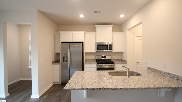 kitchen with a breakfast bar, sink, white cabinets, stainless steel appliances, and light stone countertops