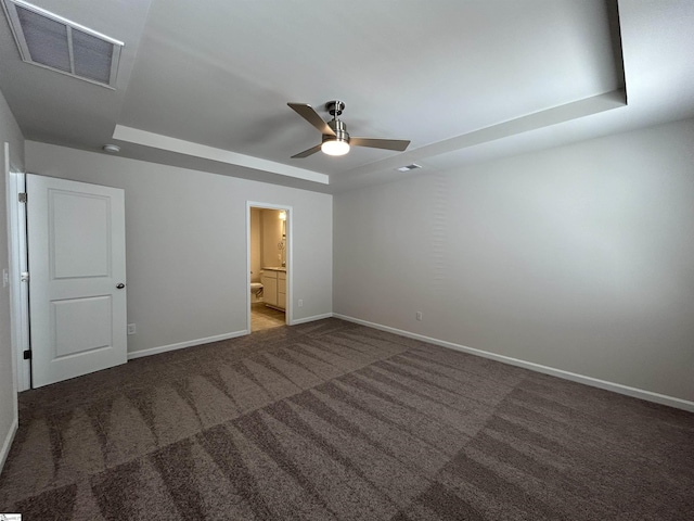 unfurnished bedroom featuring a tray ceiling, carpet floors, ensuite bath, and ceiling fan