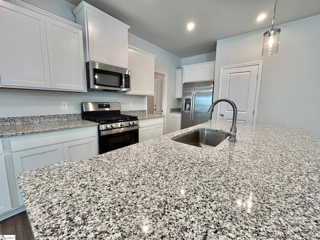 kitchen featuring sink, appliances with stainless steel finishes, white cabinetry, a kitchen island with sink, and light stone countertops