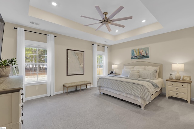 bedroom with light colored carpet, ceiling fan, and a tray ceiling