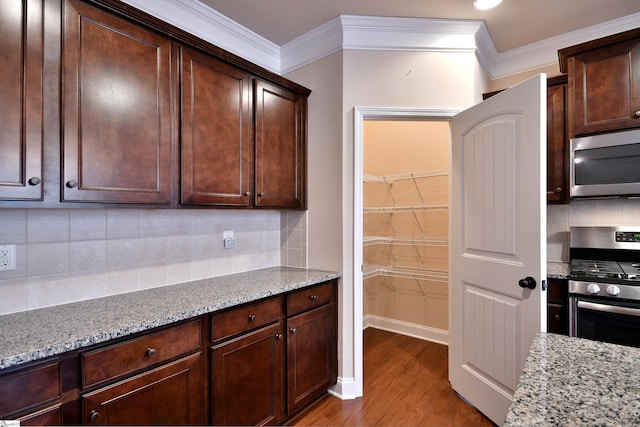 kitchen with ornamental molding, dark brown cabinetry, stainless steel appliances, light stone countertops, and light wood-type flooring