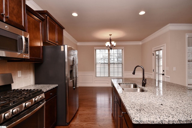 kitchen with sink, ornamental molding, a kitchen island with sink, stainless steel appliances, and light stone countertops