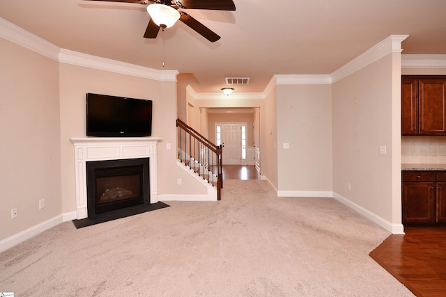 unfurnished living room featuring carpet floors, ornamental molding, and ceiling fan