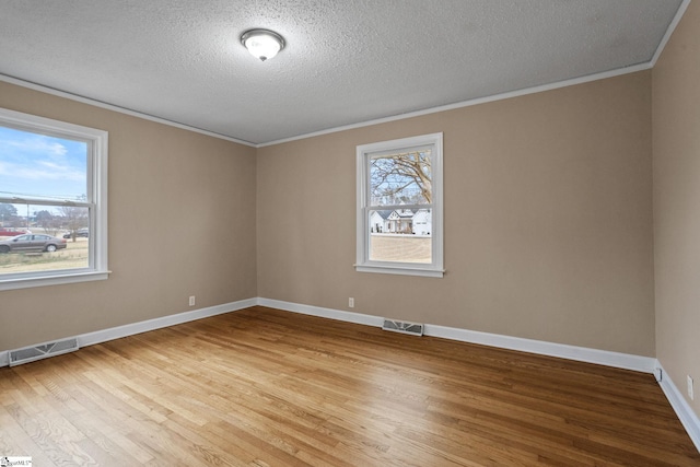 spare room featuring ornamental molding, light hardwood / wood-style floors, and a textured ceiling