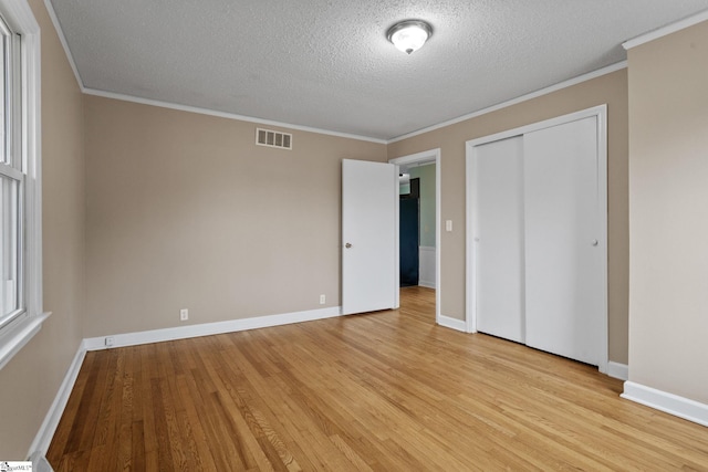 unfurnished bedroom with ornamental molding, a closet, a textured ceiling, and light hardwood / wood-style flooring