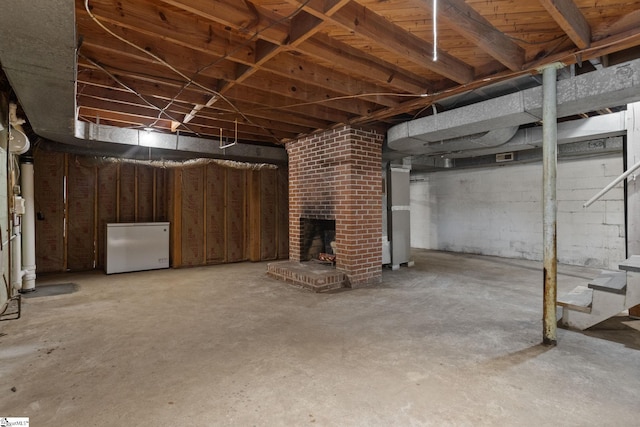 basement featuring a brick fireplace and refrigerator