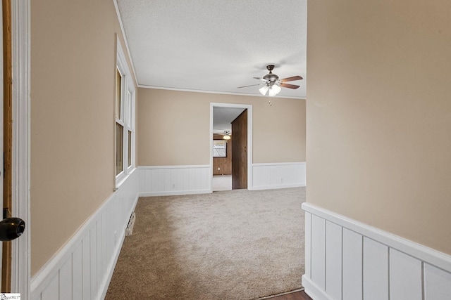 unfurnished room featuring ceiling fan, ornamental molding, carpet flooring, and a textured ceiling