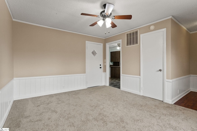 carpeted empty room with ceiling fan, ornamental molding, and a textured ceiling