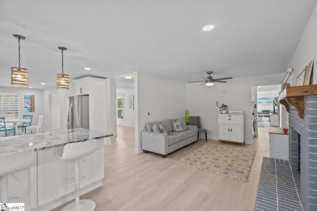 living room featuring a fireplace, ceiling fan, and light wood-type flooring