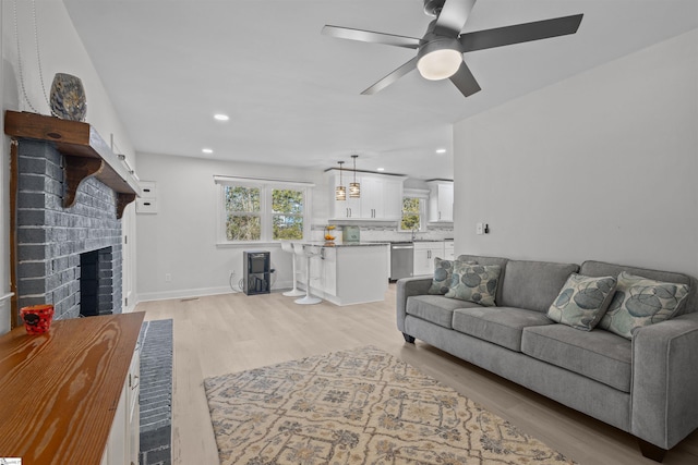 living room with ceiling fan, a brick fireplace, and light hardwood / wood-style floors