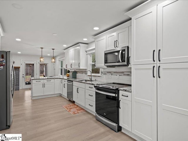 kitchen with sink, appliances with stainless steel finishes, white cabinetry, hanging light fixtures, and kitchen peninsula