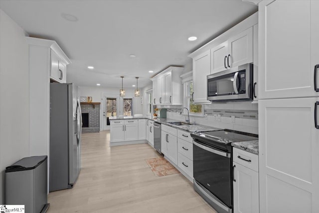 kitchen with sink, white cabinets, hanging light fixtures, stainless steel appliances, and light stone countertops