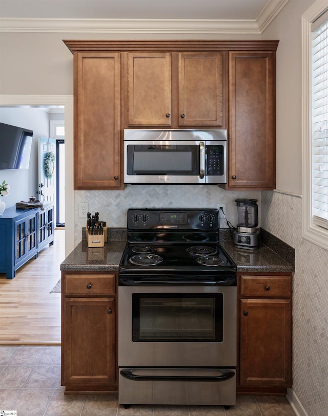 kitchen with crown molding, appliances with stainless steel finishes, dark stone counters, and light tile patterned floors