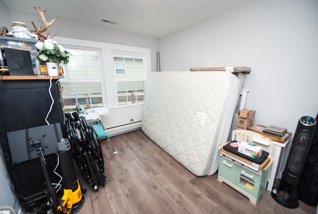 bedroom with hardwood / wood-style flooring, a baseboard radiator, and a textured ceiling