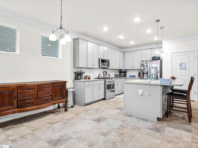 kitchen featuring appliances with stainless steel finishes, hanging light fixtures, light stone counters, a center island with sink, and decorative backsplash