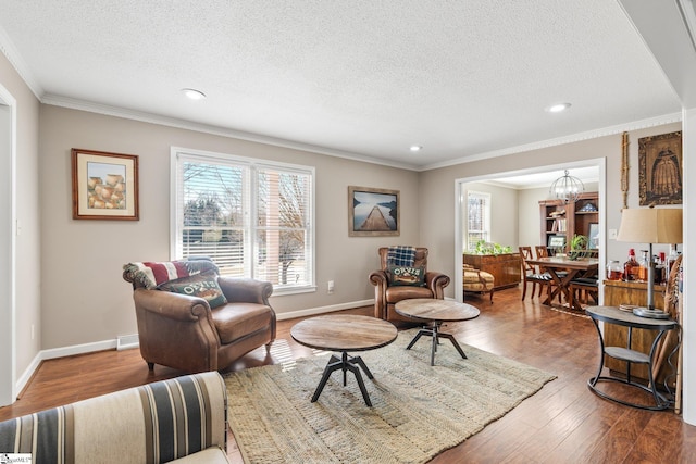 living room featuring wood-type flooring, ornamental molding, a chandelier, and a textured ceiling