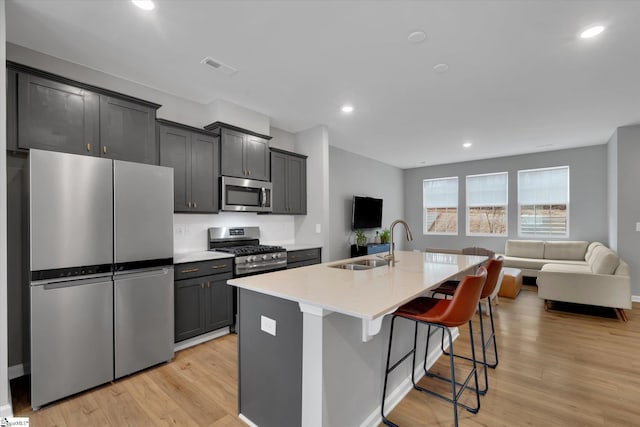 kitchen with a breakfast bar, sink, light hardwood / wood-style flooring, appliances with stainless steel finishes, and an island with sink