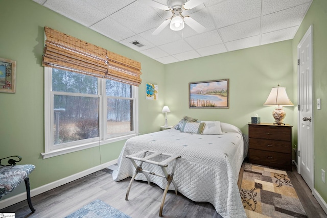 bedroom featuring ceiling fan, wood-type flooring, and a drop ceiling