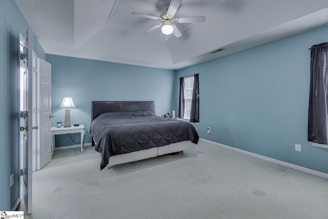 bedroom featuring ceiling fan, a tray ceiling, and light carpet