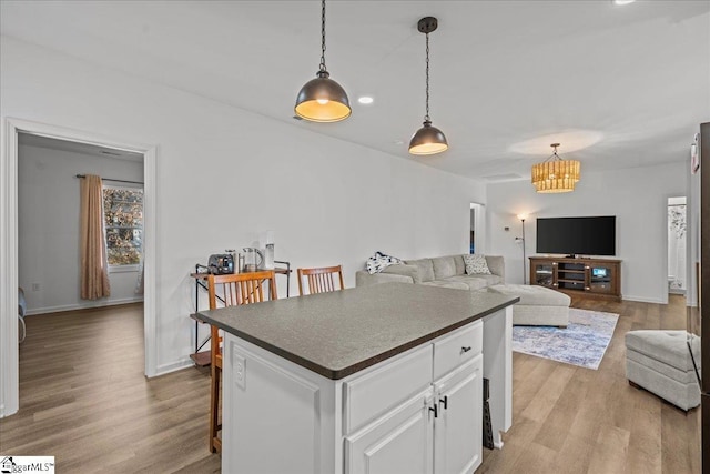 kitchen with a kitchen island, pendant lighting, white cabinetry, a kitchen bar, and light hardwood / wood-style flooring