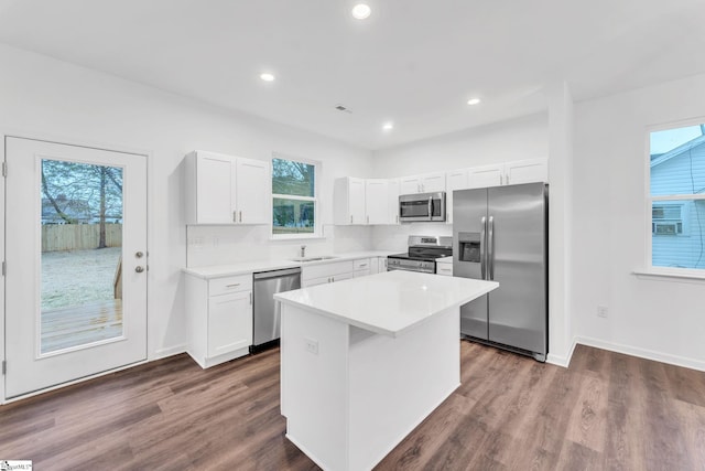 kitchen with dark hardwood / wood-style flooring, a kitchen island, white cabinets, stainless steel appliances, and backsplash