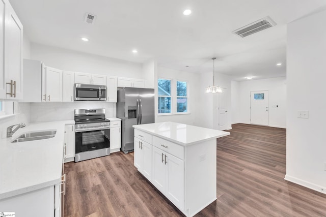 kitchen with sink, hanging light fixtures, a kitchen island, stainless steel appliances, and white cabinets