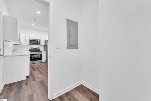 kitchen with dark hardwood / wood-style floors, electric panel, stainless steel appliances, decorative backsplash, and white cabinets