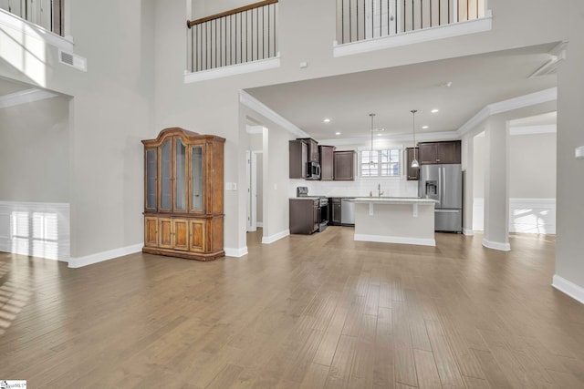 unfurnished living room featuring sink, crown molding, wood-type flooring, and a high ceiling