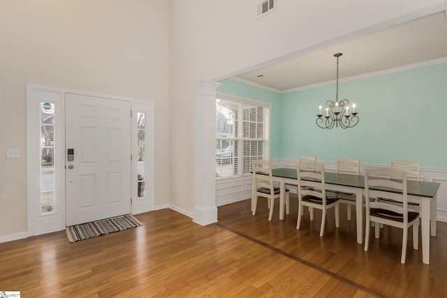 foyer entrance featuring crown molding, hardwood / wood-style flooring, a towering ceiling, a chandelier, and ornate columns