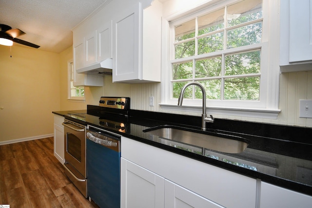 kitchen featuring sink, dark wood-type flooring, appliances with stainless steel finishes, dark stone countertops, and white cabinetry