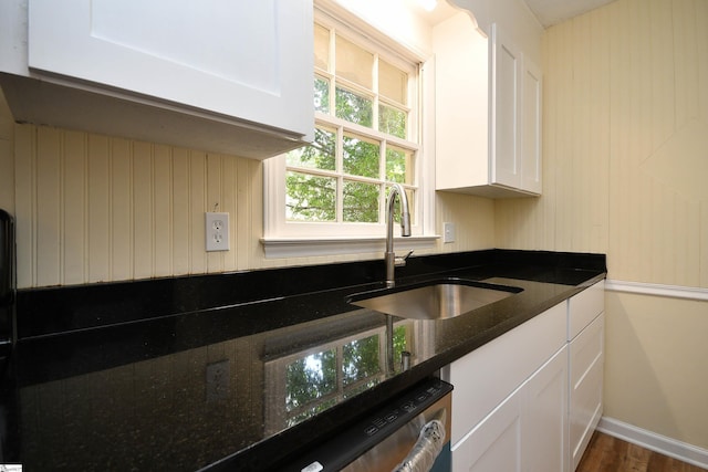 kitchen with white cabinetry, stainless steel dishwasher, dark stone counters, and sink