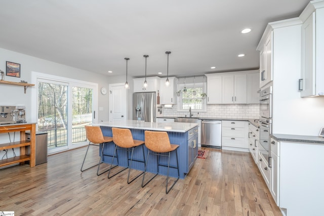 kitchen featuring appliances with stainless steel finishes, a center island, white cabinets, a kitchen bar, and decorative light fixtures