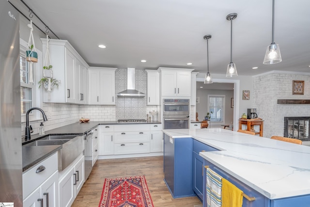 kitchen featuring blue cabinets, white cabinetry, appliances with stainless steel finishes, and wall chimney exhaust hood