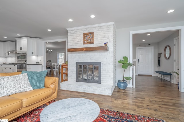 living room with an inviting chandelier, dark hardwood / wood-style flooring, and a brick fireplace