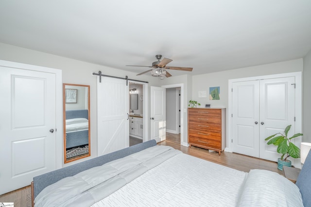 bedroom with ceiling fan, a closet, a barn door, and light hardwood / wood-style flooring