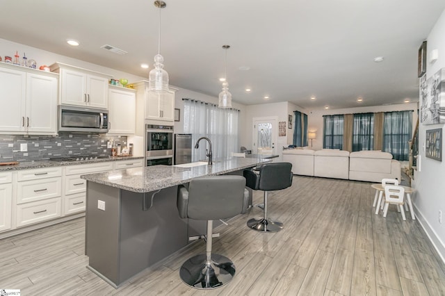 kitchen featuring appliances with stainless steel finishes, hanging light fixtures, a kitchen breakfast bar, white cabinets, and a center island with sink