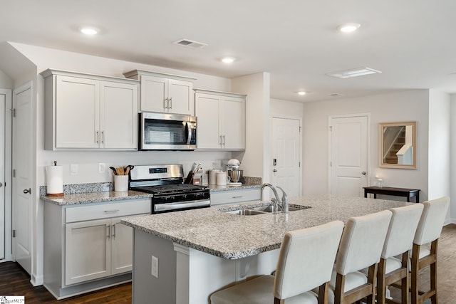 kitchen featuring light stone countertops, appliances with stainless steel finishes, a kitchen island with sink, and sink