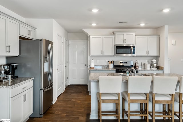 kitchen featuring white cabinetry, light stone counters, a center island with sink, appliances with stainless steel finishes, and dark hardwood / wood-style floors