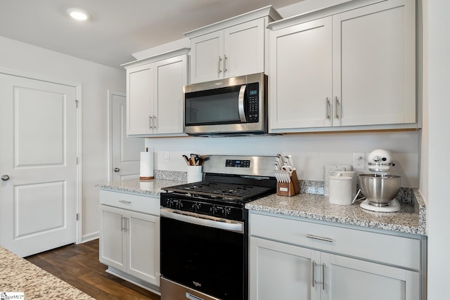 kitchen featuring dark hardwood / wood-style flooring, light stone countertops, white cabinets, and appliances with stainless steel finishes