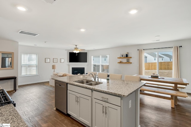 kitchen featuring appliances with stainless steel finishes, sink, light stone counters, dark wood-type flooring, and a center island with sink