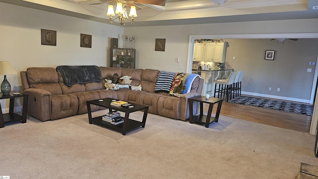 living room with ceiling fan, coffered ceiling, ornamental molding, light colored carpet, and beamed ceiling