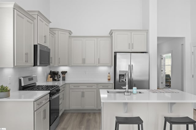 kitchen with backsplash, stainless steel appliances, a breakfast bar area, and gray cabinetry