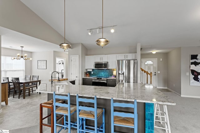 kitchen featuring sink, white cabinetry, stainless steel appliances, light stone countertops, and decorative light fixtures