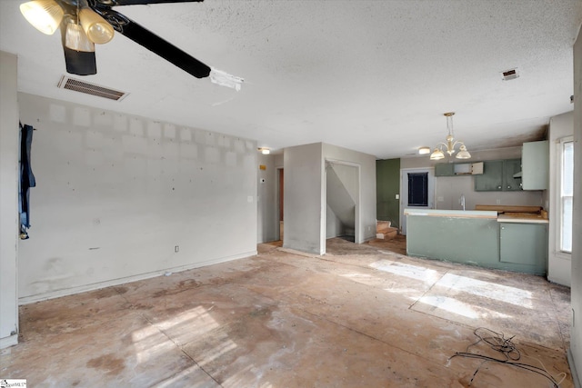 unfurnished living room with ceiling fan with notable chandelier and a textured ceiling