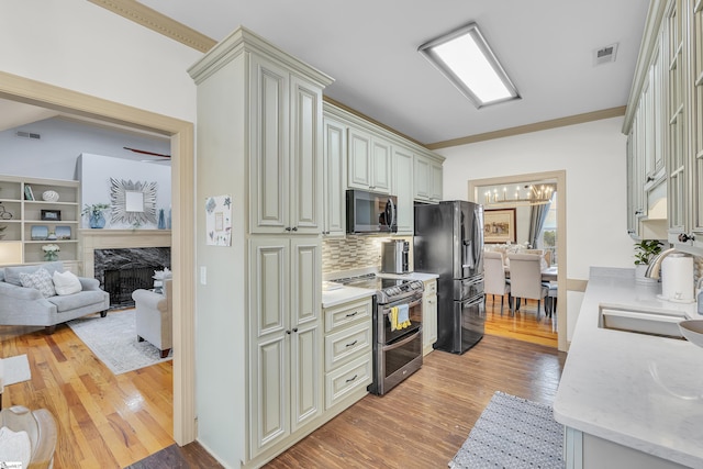 kitchen featuring sink, light hardwood / wood-style flooring, a premium fireplace, appliances with stainless steel finishes, and backsplash